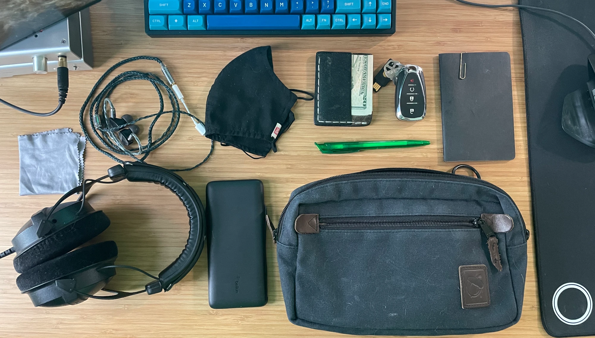 Top down picture of a desk showing, wallet, keys, headphones, and bag.